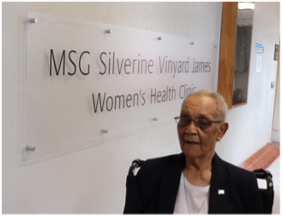 Photo of Silverine James standing beside the sign bearing her name inside the Salvem Virginia clinic